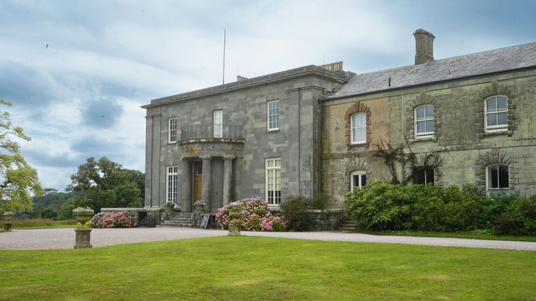 Looking across a lawn at a mansion with a cloudy sky behind.